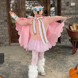 Girl wearing owl costume on her front porch, spreading her colorful layered cape with matching felt owl mask, fluffy white leg warmers, and tutu, smiling as she poses for the camera.