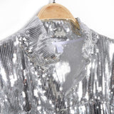 Close-up of silver sequin fringe jacket with popped collar on a wooden hanger against a white background. Elegant details for a glamorous wardrobe addition.
