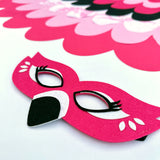 Close-up details of felt flamingo mask with patterned fabric cape against white background.
