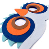 Close-up details of felt owl mask against white background with intricately cut layers of white, blue, and orange felt stitched together.