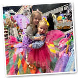Heartwarming image of two little girls, hugging and joyfully posing for a photo, adorned in their new Knotty Kid Butterfly Costume Wing Sets. 